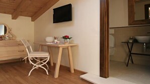 Une chambre à coucher avec une commode en bois, une coiffeuse avec un miroir, une chaise et une petite table sur laquelle est posé un vase de fleurs.