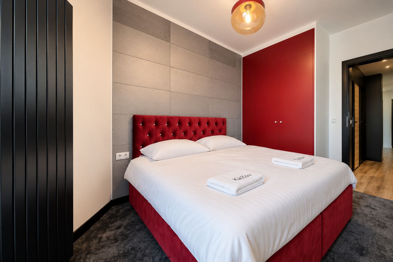A hotel room with a large bed, a red headboard, and a grey tiled wall.