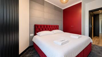 A hotel room with a large bed, a red headboard, and a grey tiled wall.