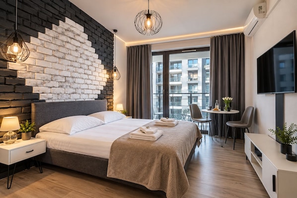 Habitación de hotel moderna con cama, mesita de noche, lámpara y vistas amplias a la ciudad.