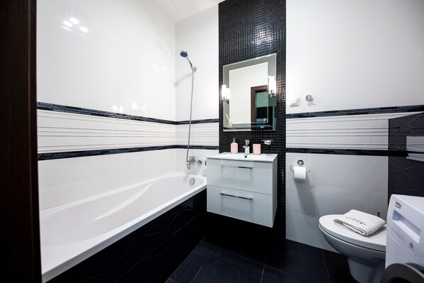 A modern bathroom with a white bathtub, a sink with a mirror, and a toilet.