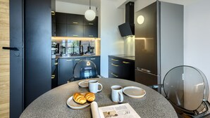A modern kitchen with dark cabinetry, a round dining table with croissants, coffee cups, and a newspaper. - Kazou Residence Burakowska (Warsaw)