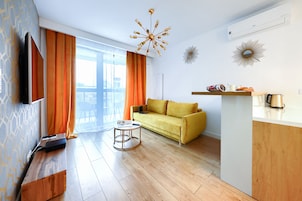 A modern living room with a yellow sofa, a coffee table, a flat-screen TV, and a wooden sideboard.