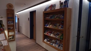 A hallway with wooden bookshelves filled with books, a wooden display case with postcards, and a wooden counter with brochures. - Berggasthof Sonne Imberg (Sonthofen)