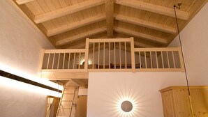 A room with a sloped wooden ceiling, a ladder, a bed, and a wall-mounted light fixture. - Berggasthof Sonne Imberg (Sonthofen)