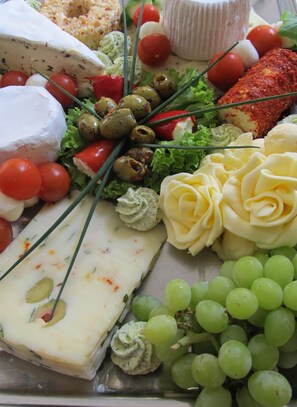 A cheese platter with various cheeses, grapes, cherry tomatoes, and olives. - Pension Elli Krossner (Hartmannsdorf)
