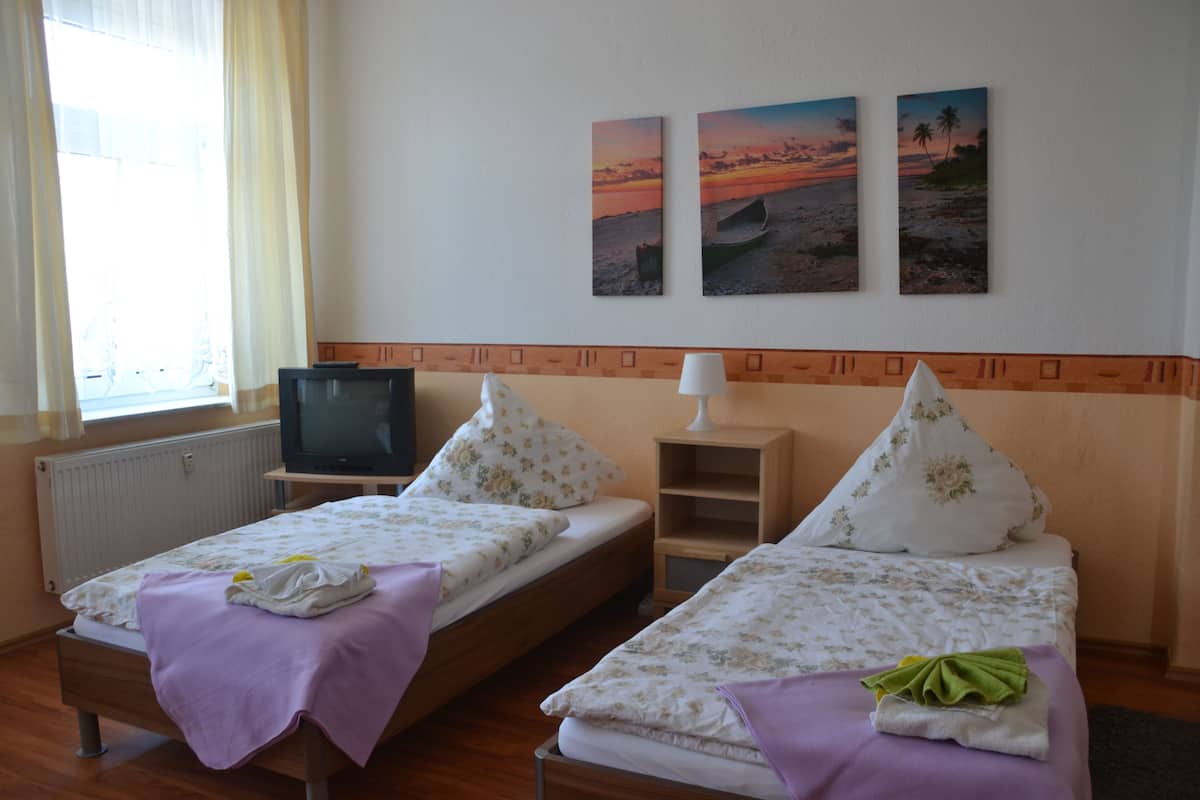 A hotel room with two single beds, a television, a window with curtains, and three wall-mounted sunset paintings.