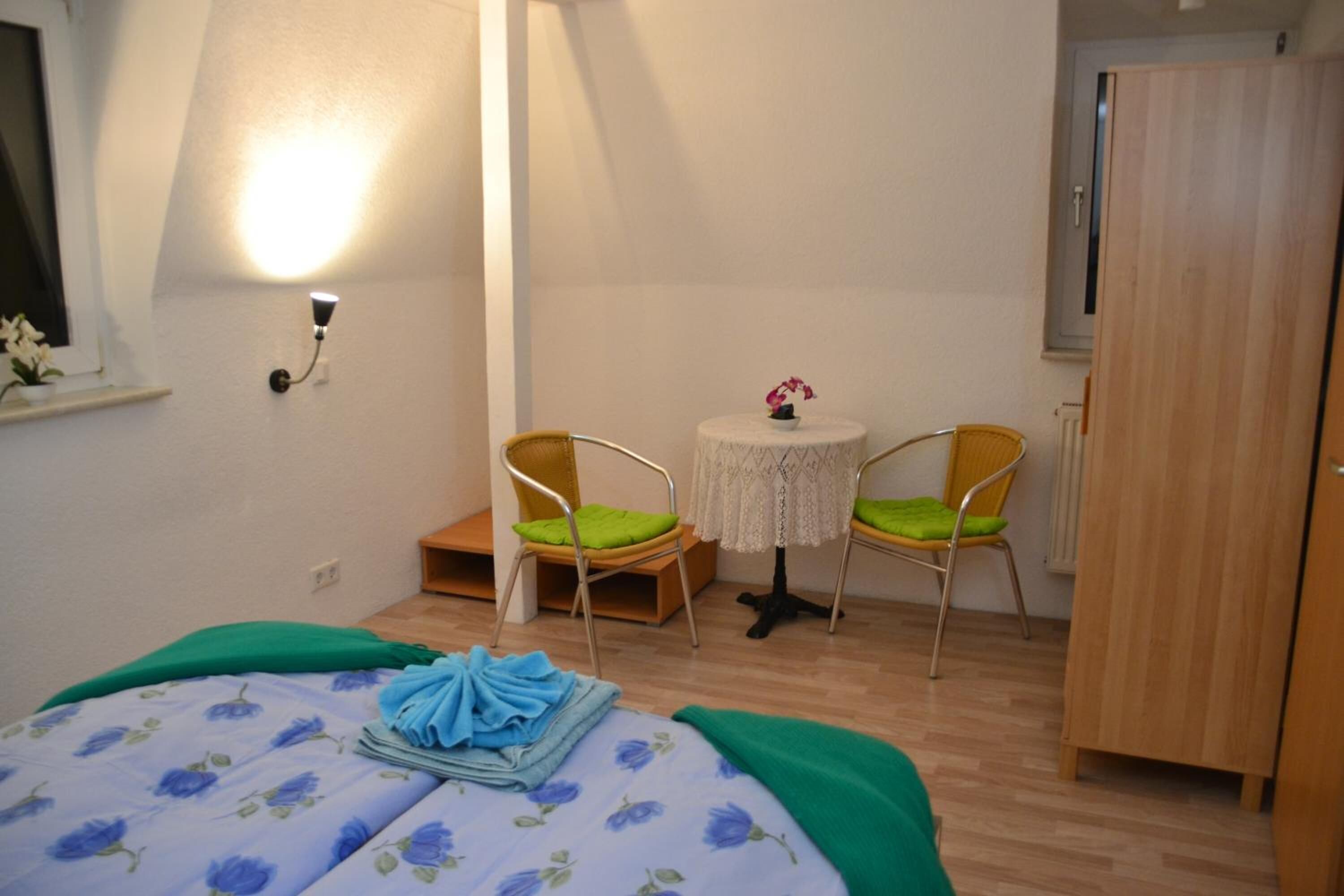 A bedroom with a bed, two chairs, a small table, and a wardrobe.