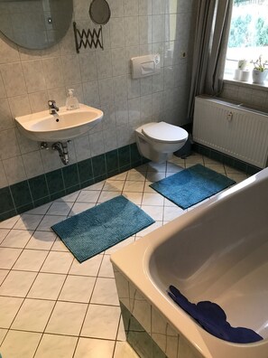 A bathroom with a bathtub, a sink, a toilet, and two blue mats on the floor. - Pension Elli Krossner (Hartmannsdorf)