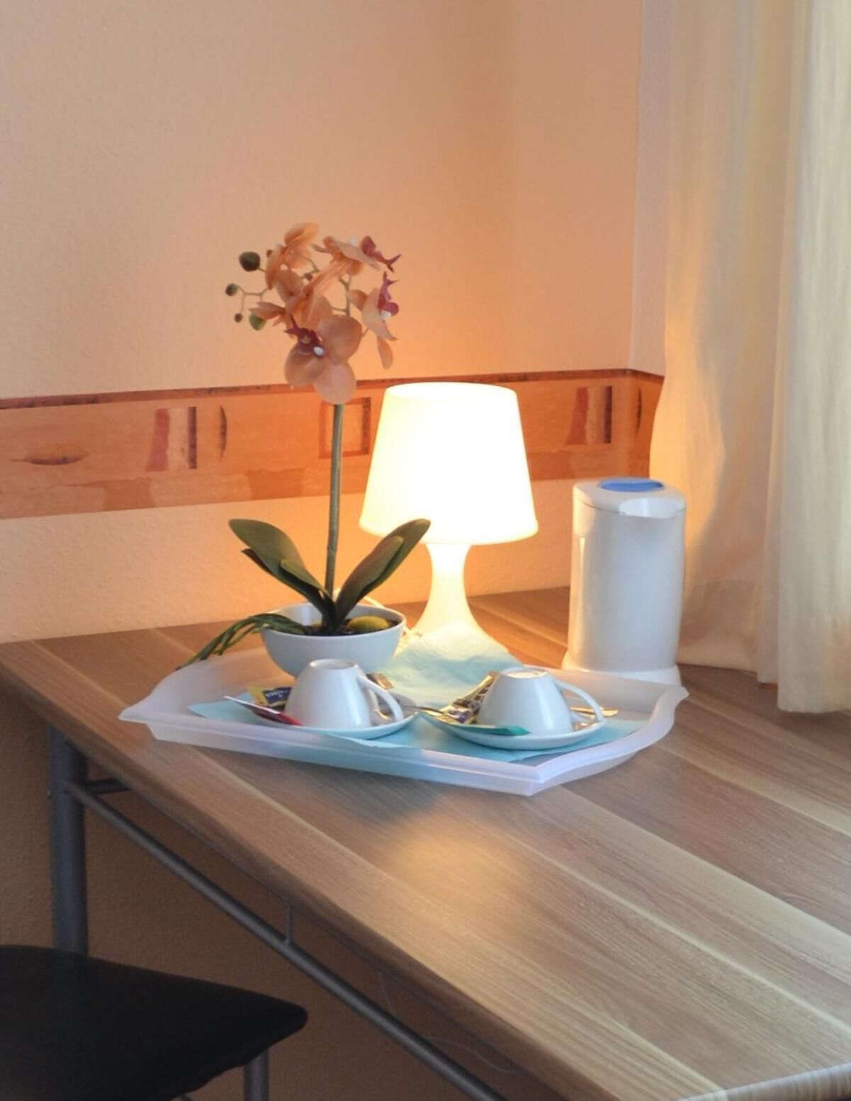 Ein Hotelzimmer mit Schreibtisch aus Holz, einem Blumentopf, einer Tischlampe und einem Tablett mit Tassen und einer kleinen Schale.