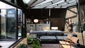 Un interior moderno con un gran ventanal que da a un balcón, un sofá modular, sillas de madera y un comedor con barra.