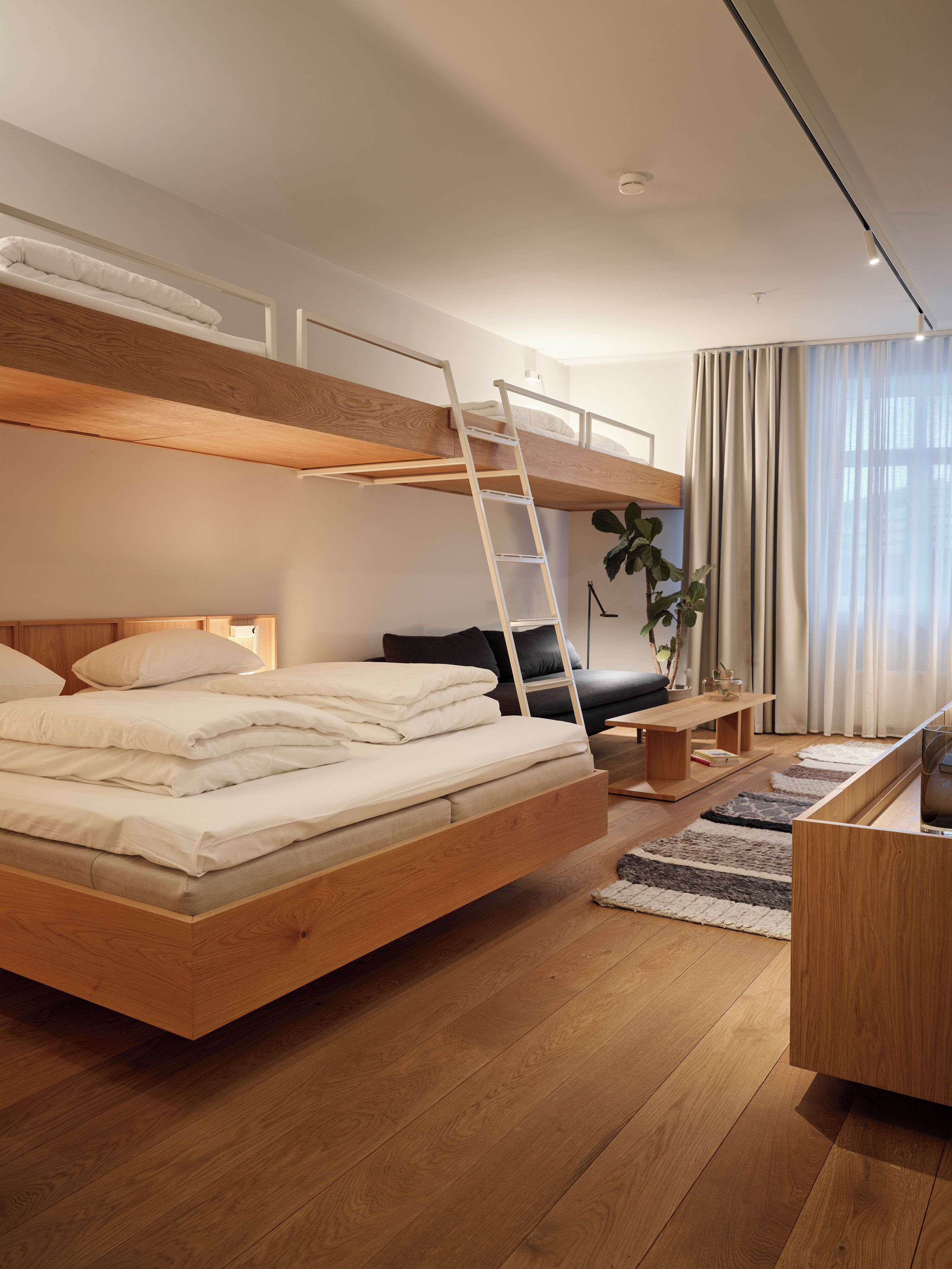 A modern bedroom with a wooden bunk bed, a desk, a chair, and a potted plant.
