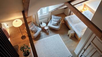 A loft bedroom with a high ceiling, exposed beams, a bed, a sofa, a small table, and a potted plant.
