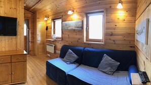 A wooden cabin interior with a sofa, a television, and a window with blinds. - Astoria (Broadstairs)