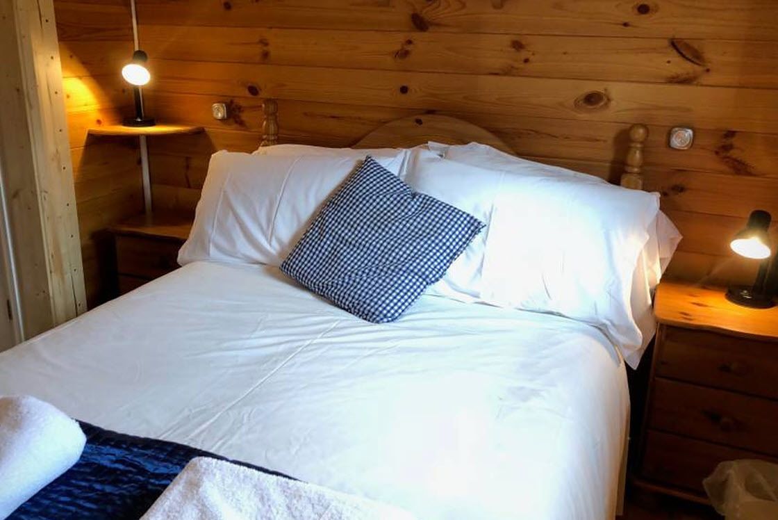 A wooden cabin-style room with a bed, white linens, and a checkered pillow.