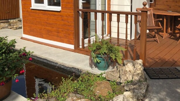 A wooden cabin with a deck, a small garden, and a satellite dish. - Astoria (Broadstairs)