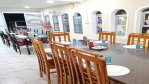 A dining area with wooden chairs and tables, a 'Welcome' sign, and artwork on the walls. - Victoria Guest House (Pasikuda)