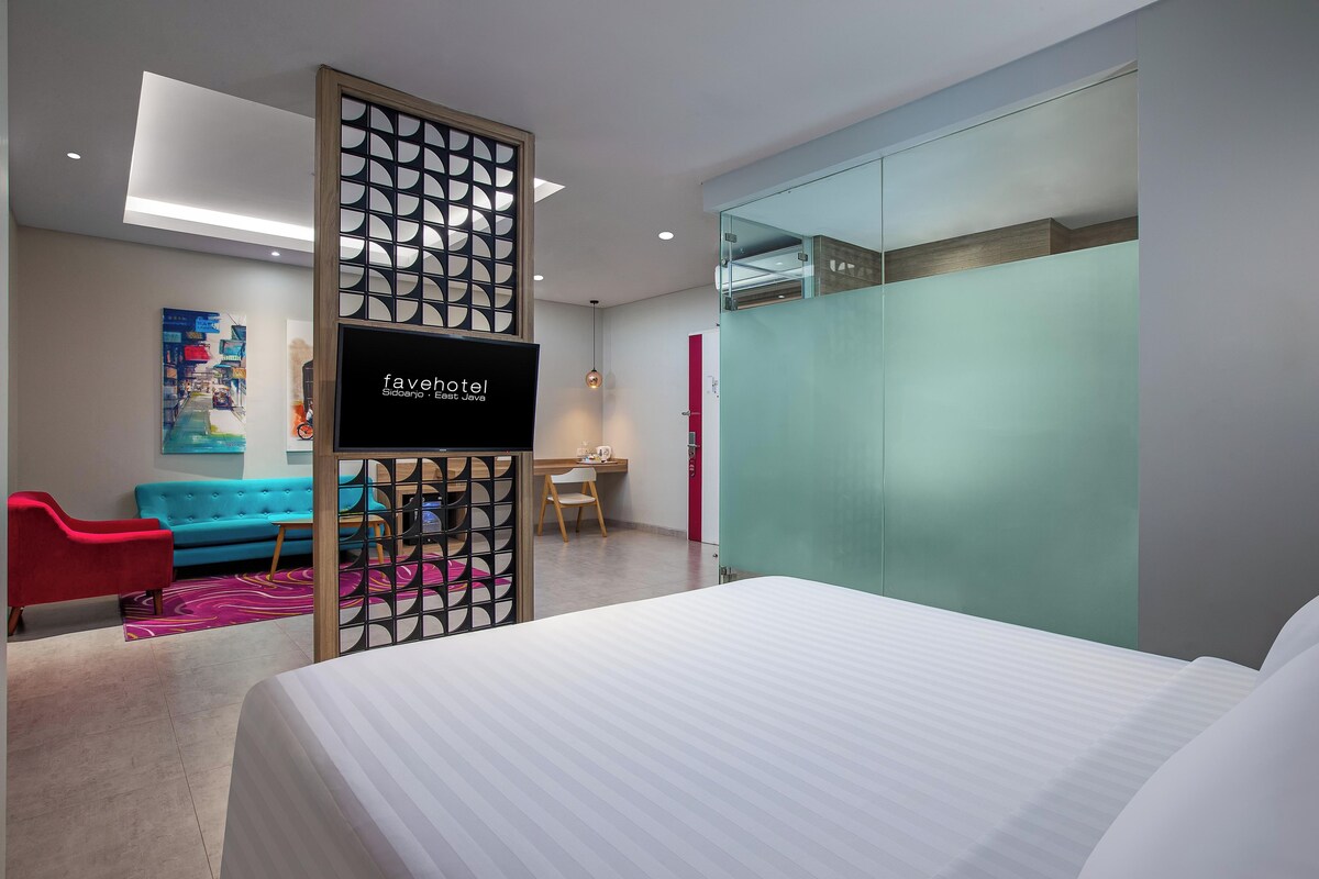 A modern hotel room with a bed, a desk, a chair, a sofa, and a TV.