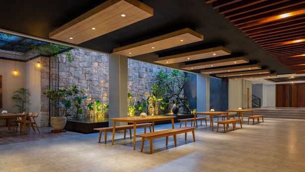 Un espacio interior amplio con mesas y bancos de madera, paredes de piedra y un diseño de techo moderno.