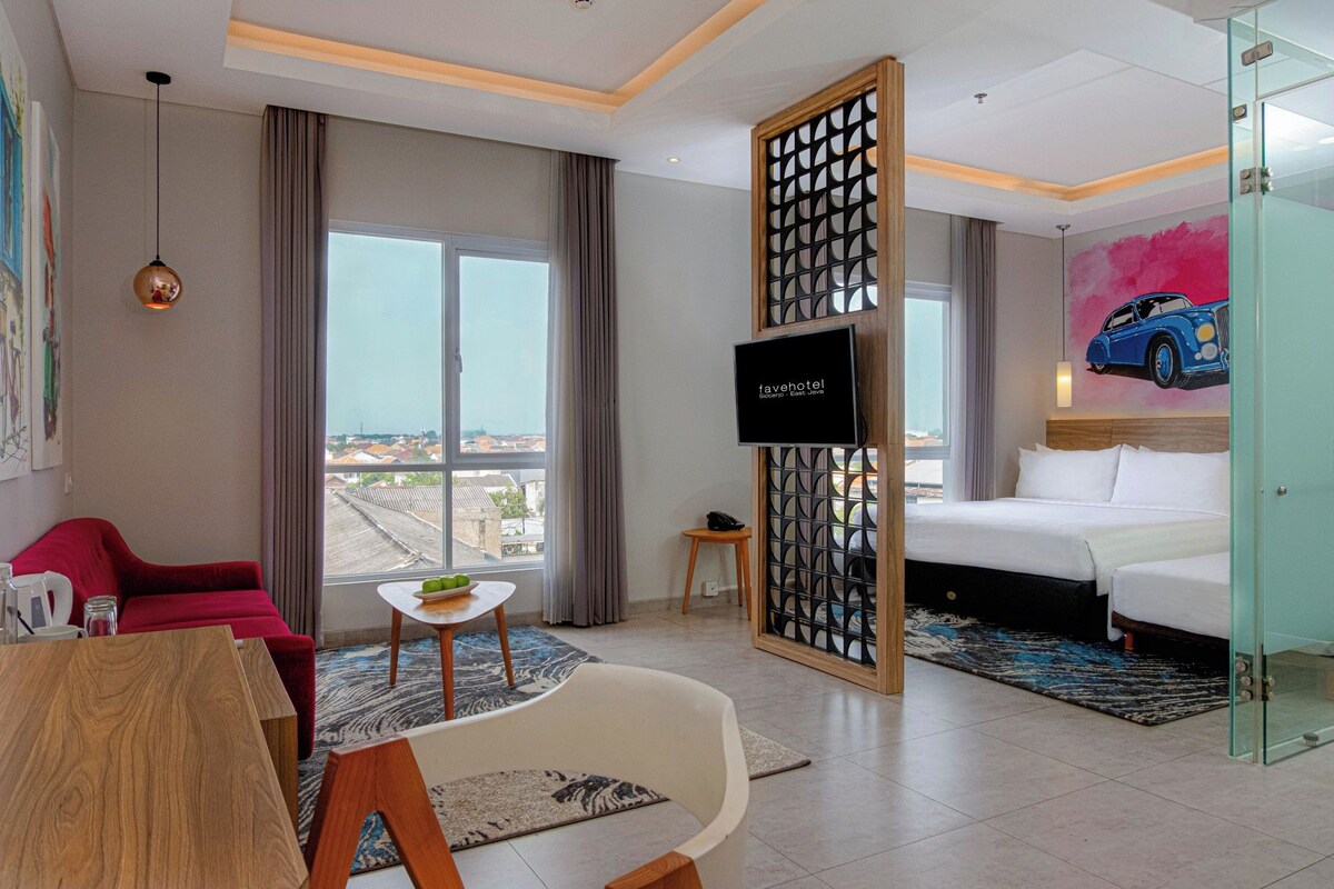 A hotel room with a bed, a desk, a chair, a TV, and a view of the city.