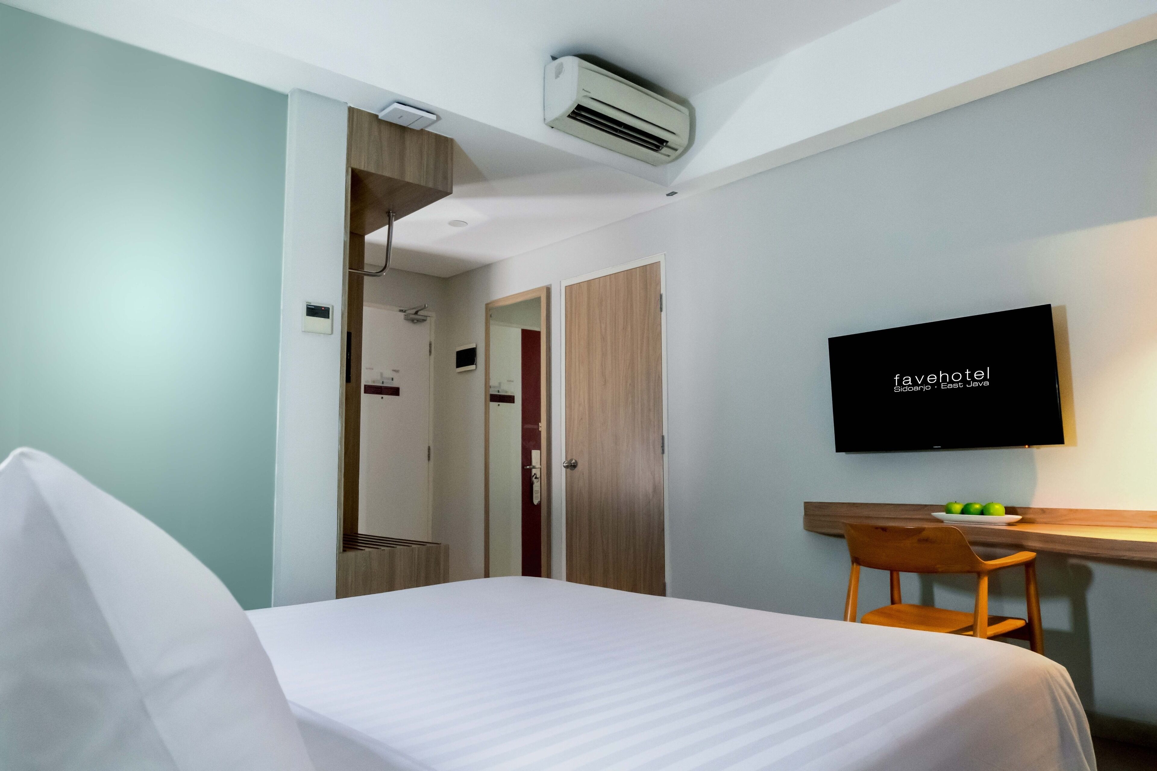 A hotel room with a bed, a desk with a chair, a television, and an air conditioning unit.
