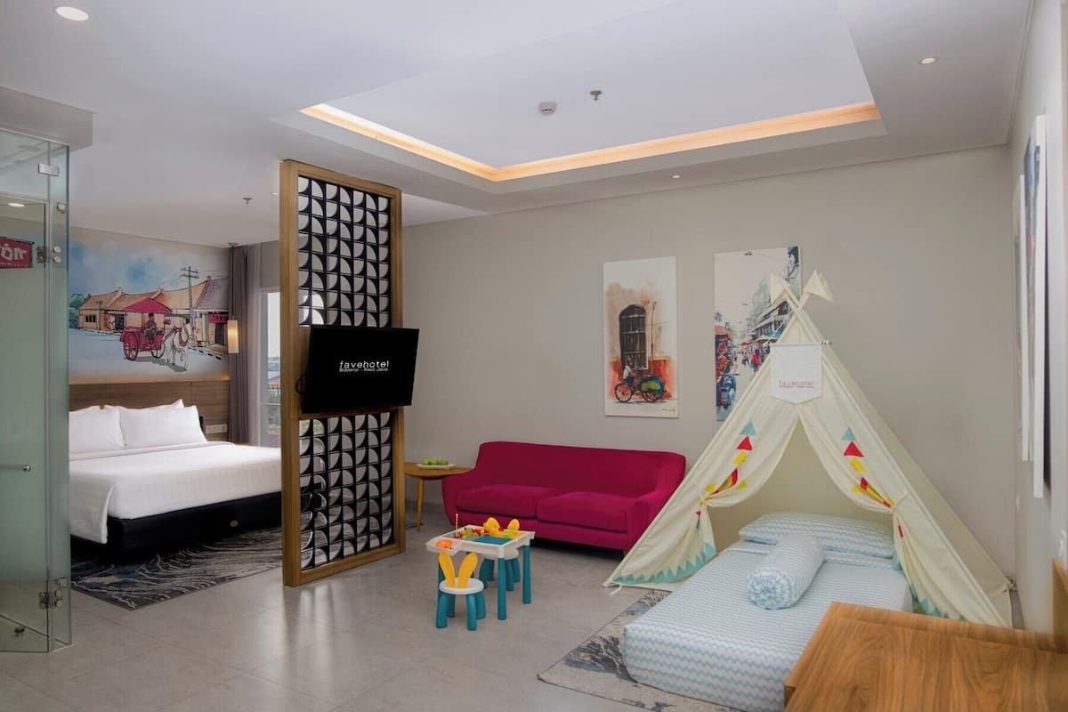 Habitación de hotel con cama, sofá rojo, una tienda de campaña, televisor y obras de arte en las paredes.
