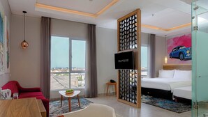 Habitación de hotel con cama, escritorio, silla, televisión y vista a la ciudad.