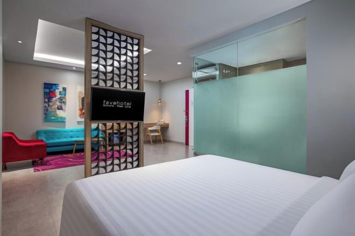 Una habitación de hotel moderna con una cama, un escritorio, una silla y una obra de arte colorida en la pared.