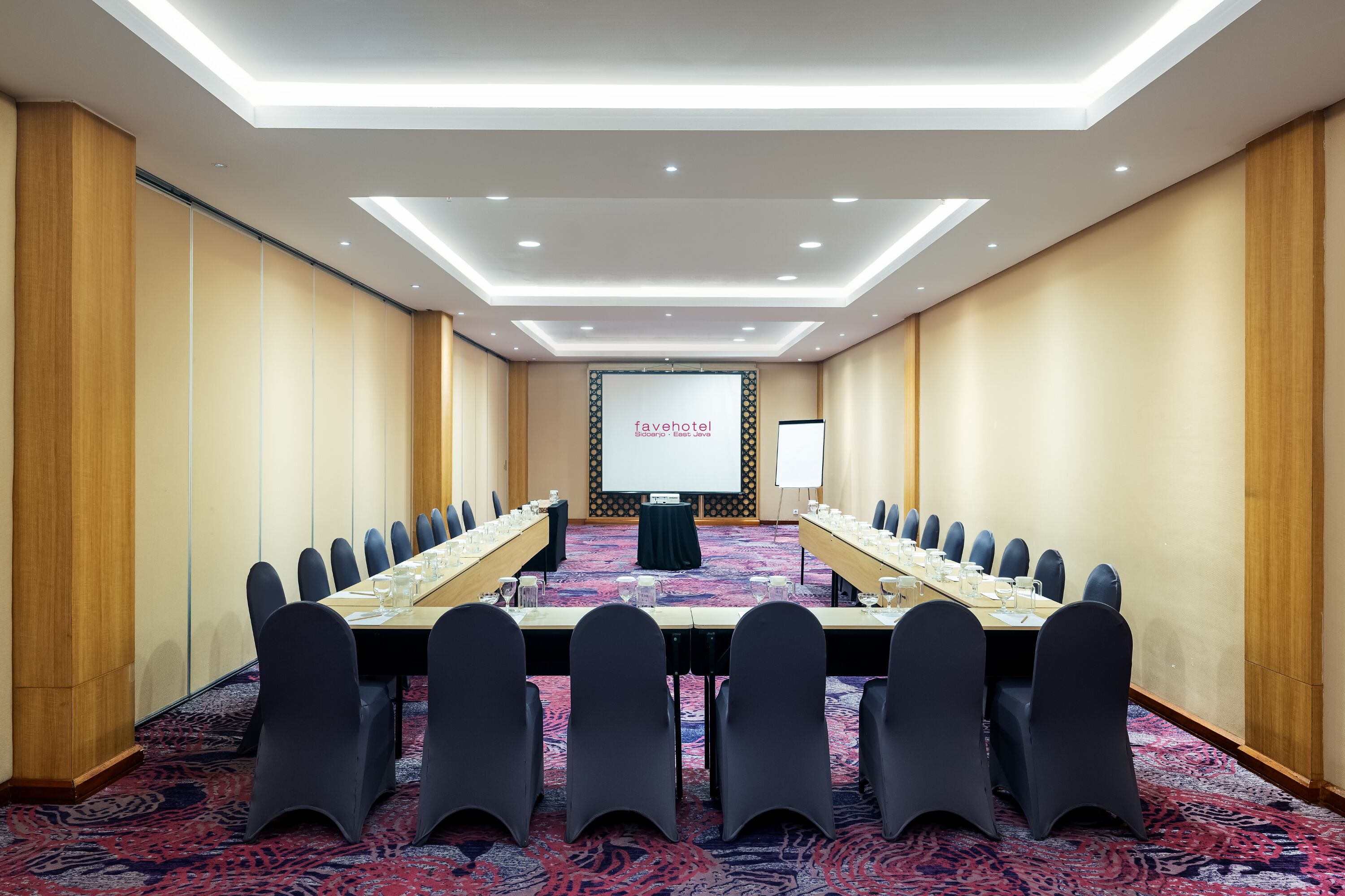 A conference room with a long table, chairs, a projector screen, and a whiteboard.