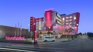 Un hotel moderno con un llamativo letrero de 'favehotel', una entrada bien iluminada y un coche estacionado frente a él.