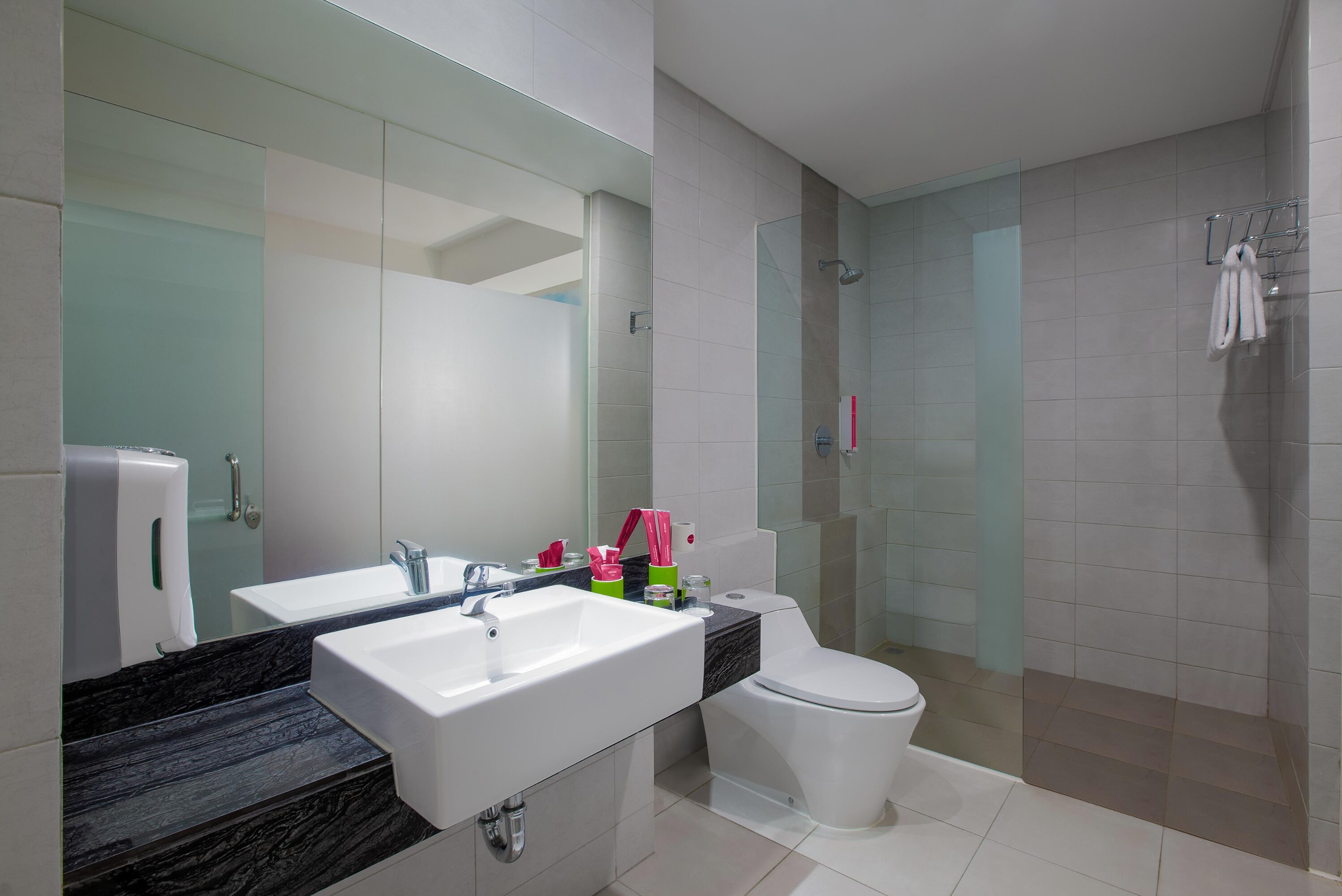 A modern bathroom with a large mirror, two sinks, a toilet, and a glass shower enclosure.