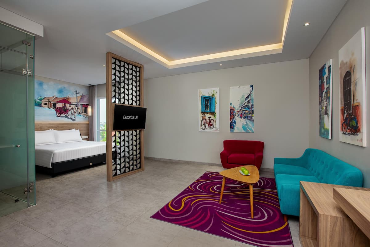 Una habitación de hotel moderna con una cama, un sofá rojo, un sofá verde azulado, una mesa de centro de madera y una alfombra colorida.