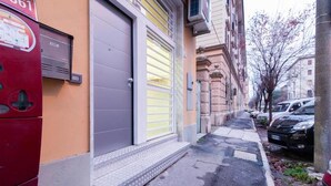 A narrow street with parked cars and a building with a closed shutter. - Freccia Rossa Bologna Apartment (Bologna)