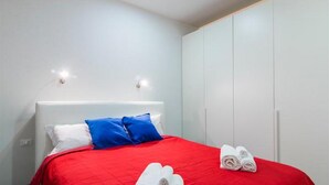 A hotel room with a red bedspread, white pillows, and two rolled towels on the bed. - Freccia Rossa Bologna Apartment (Bologna)