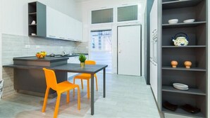A modern kitchen with a dark countertop, two orange chairs, and a white door in the background. - Freccia Rossa Bologna Apartment (Bologna)