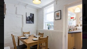 A dining area with a wooden table and chairs, a window with a view, and a kitchen visible through an open doorway. - Prospect Place (Canterbury)