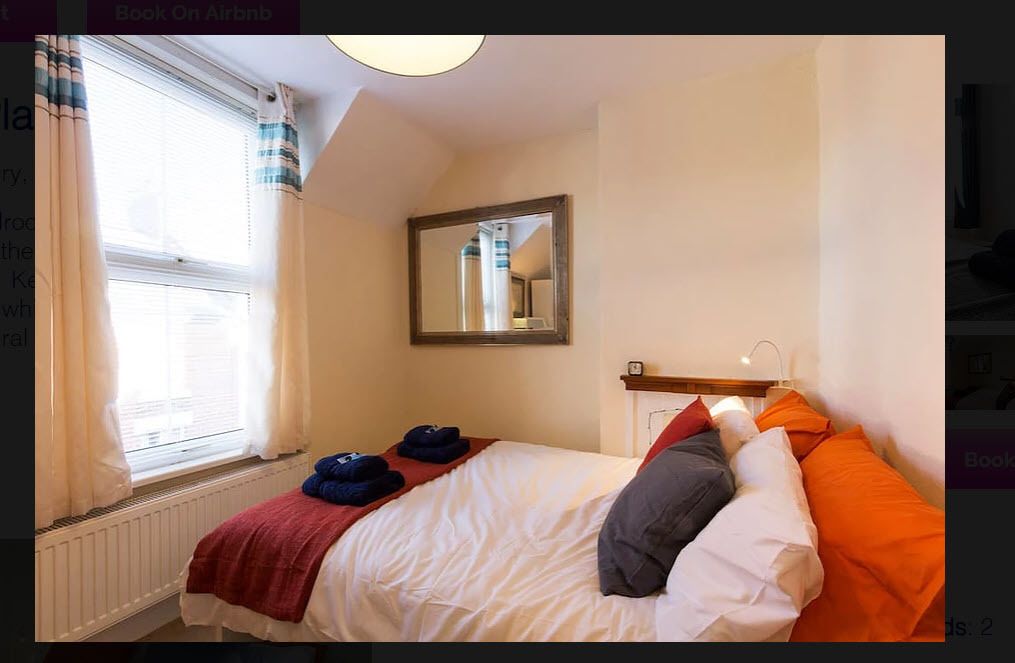 A bedroom with a bed, a window with curtains, a mirror, and a radiator.
