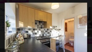 A modern kitchen with wooden cabinets, a black countertop, and a tiled backsplash. There are jars on the counter and a small plant. - Prospect Place (Canterbury)