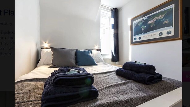 A hotel room with a neatly made bed, a framed picture on the wall, and a window with curtains. - Prospect Place (Canterbury)