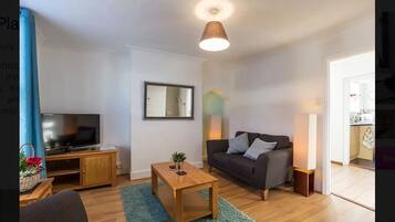 A modern living room with a flat-screen TV, a sofa, a coffee table, and a small side table.