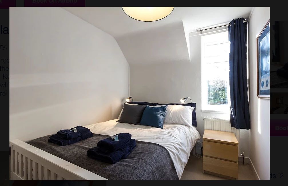 A bedroom with a bed, bedside table, and a window with curtains.