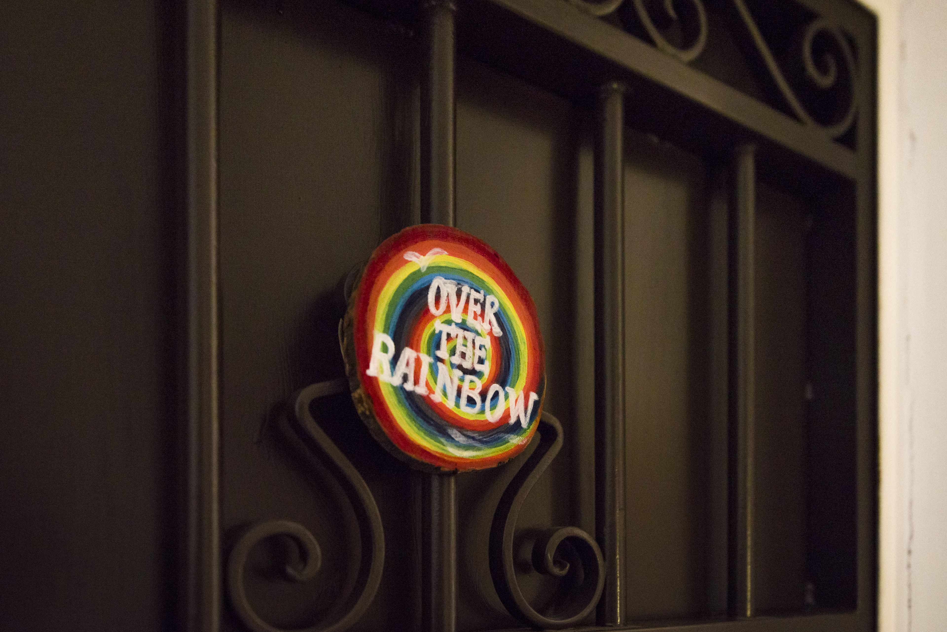 Een rond bord met de tekst 'OVER THE RAINBOW' op een metalen constructie.