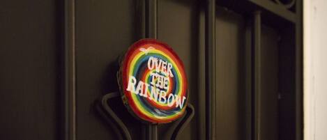 Een rond bord met de tekst 'OVER THE RAINBOW' op een metalen constructie.