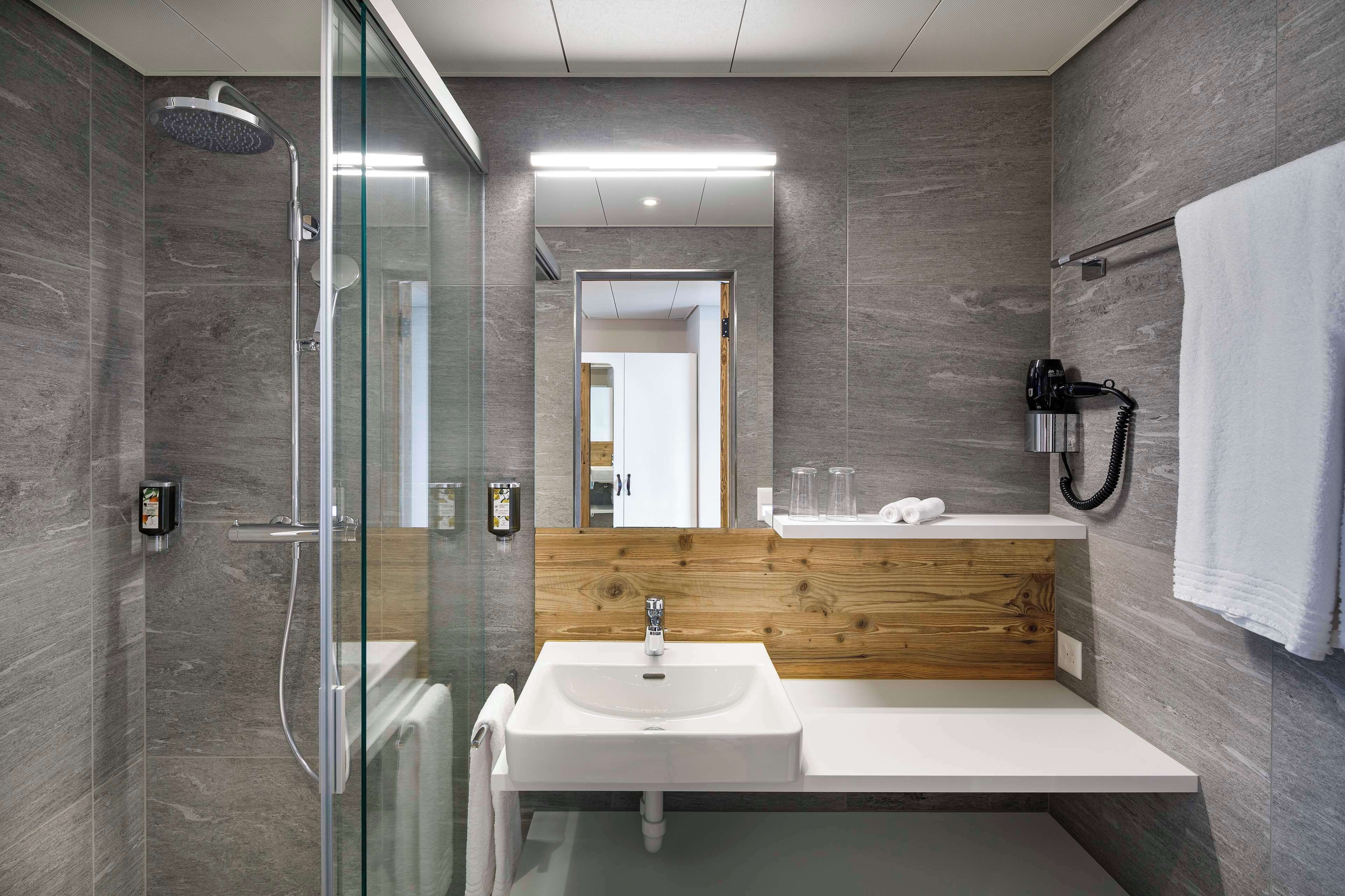Un baño moderno con ducha envuelta en vidrio, tocador de madera y lavamanos blanco.