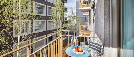 A balcony with a table set for two, featuring a plate with apples and bottles, surrounded by metal chairs and a railing.