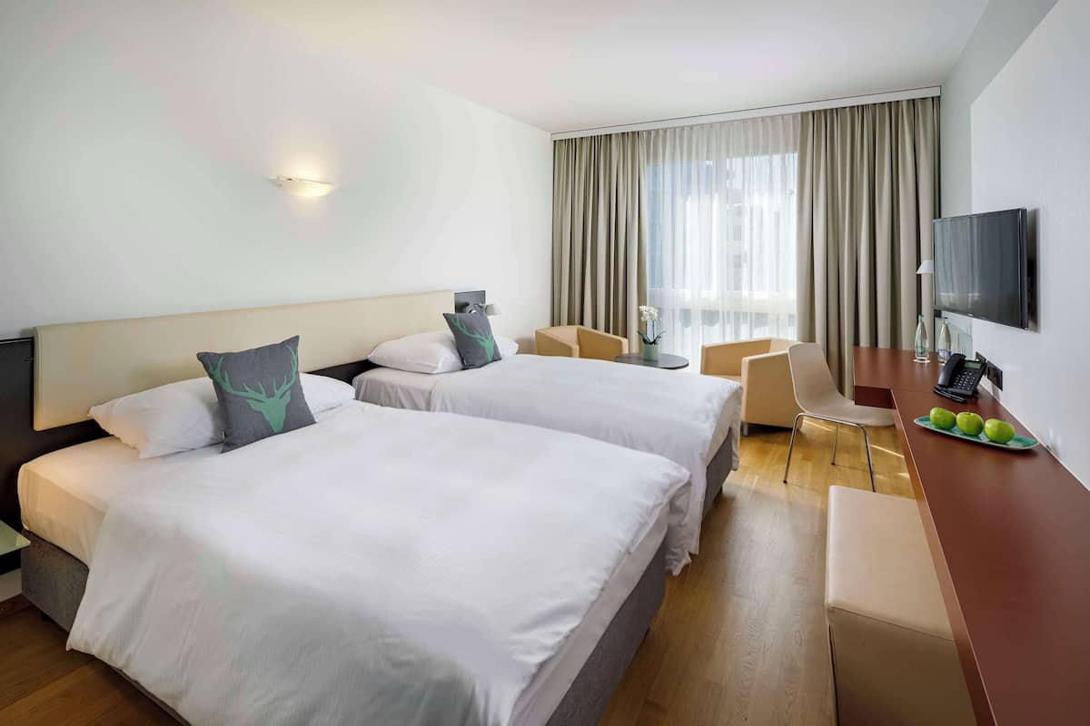 A hotel room with two beds, a desk with a TV, and a window with curtains.