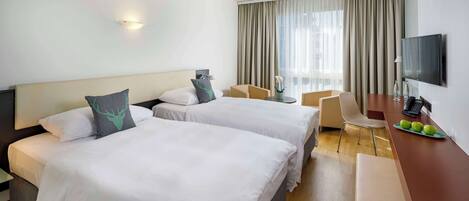 Habitación de hotel con dos camas, un escritorio con televisor y una ventana con cortinas.