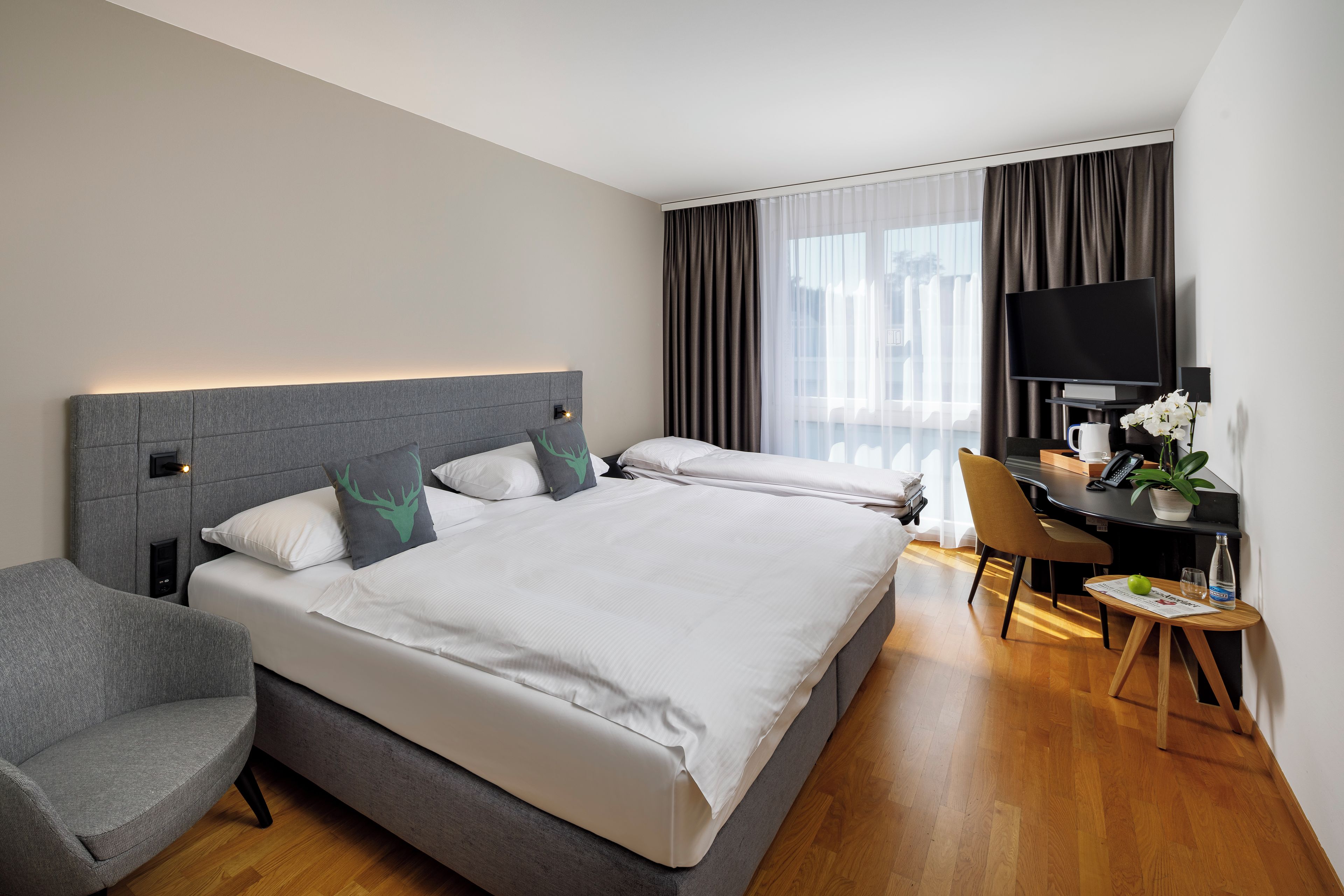 A hotel room with a bed, a desk, a chair, a television, and a window with curtains.
