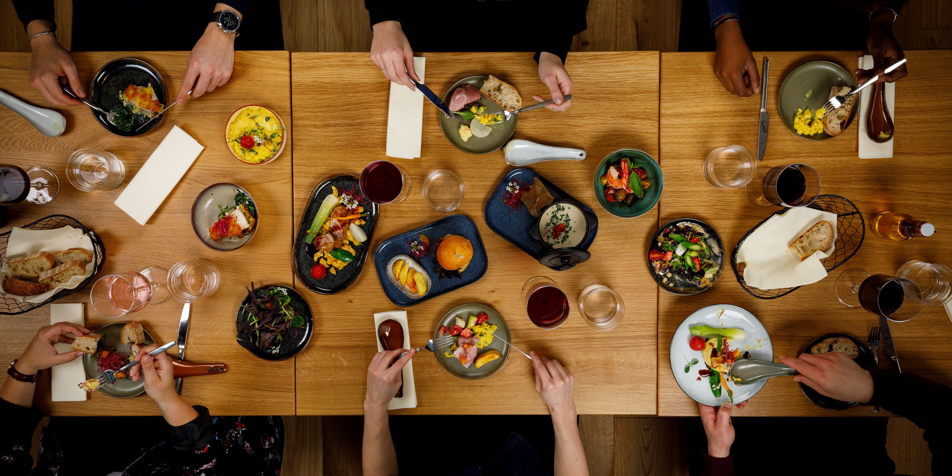 A group of people dining at a wooden table with various dishes and drinks.