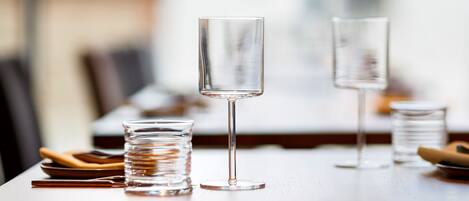 Una mesa de comedor con vasos transparentes y un vaso alto, junto con platos y cubiertos.